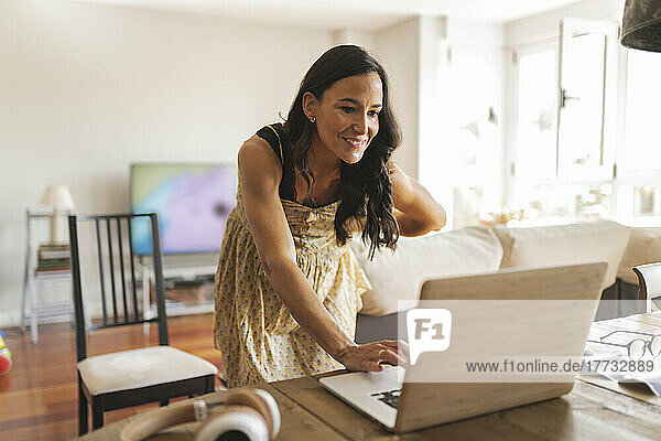 Lächelnde schwangere Frau  die von zu Hause aus mit einem Laptop arbeitet
