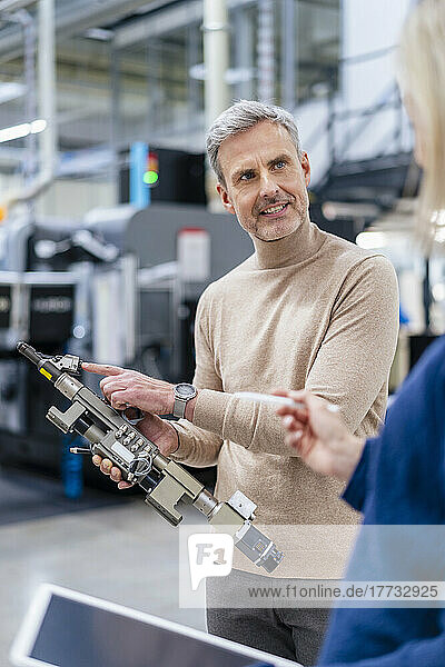 Businessman with device talking to colleague in factory