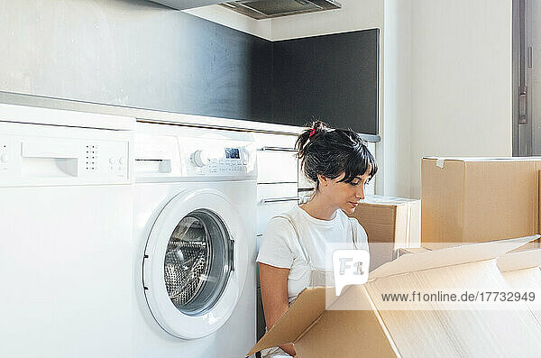 Woman looking in cardboard box sitting by washing machine in utility room