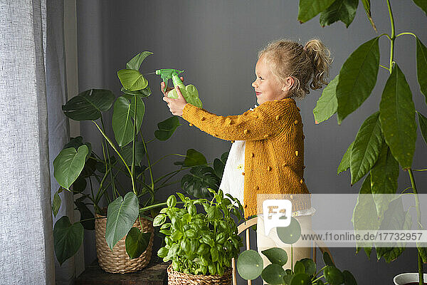 Girl spraying water on potted plants at home