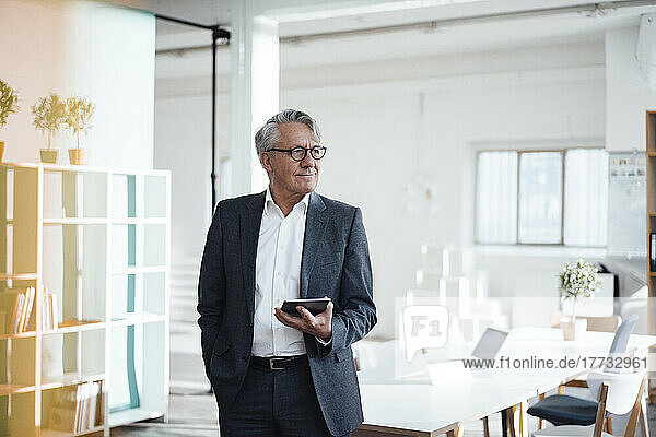 Smiling businessman holding tablet PC standing in office