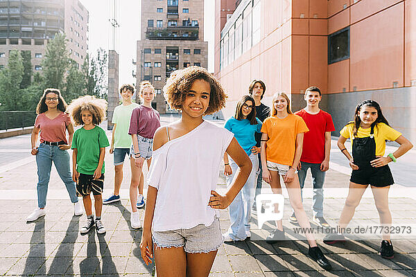 Smiling Afro girl standing with hand on hip in front of friends