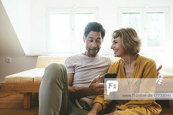 Happy woman looking at man using smart phone at home