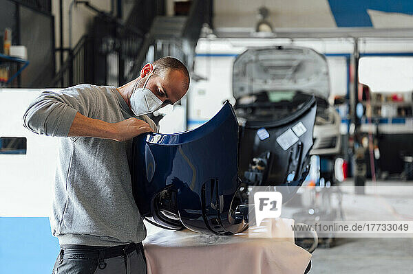 Auto mechanic examining bumper in repair shop