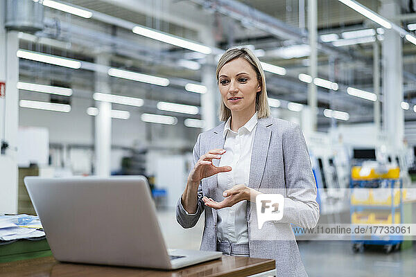 Businesswoman gesturing during video call on laptop in factory