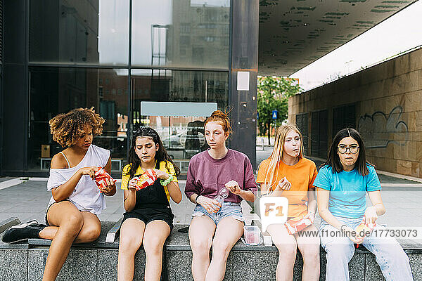 Gemischtrassige Freunde sitzen vor dem Gebäude und essen Snacks