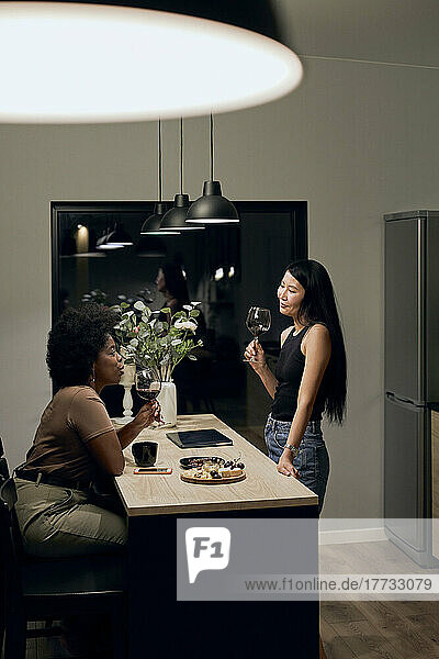Girlfriends with wineglasses talking with each other in kitchen at home