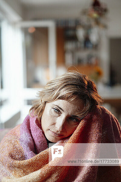 Thoughtful mature woman wrapped in blanket sitting at home