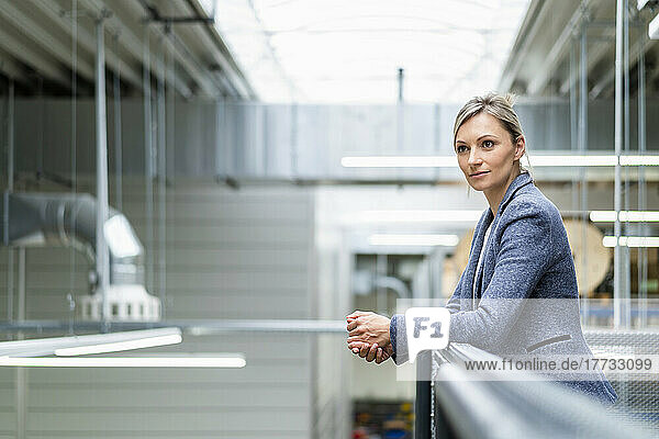 Businesswoman leaning on railing in factory