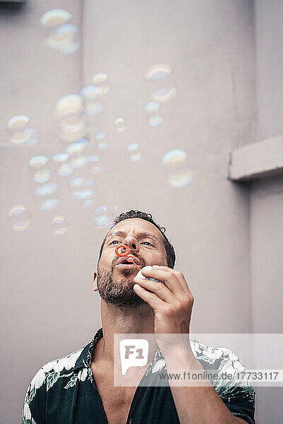 Mature man blowing bubbles in front of wall