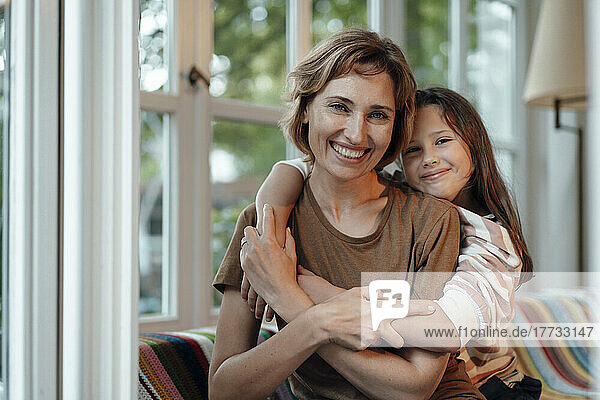 Happy girl with mother sitting in front of window at home