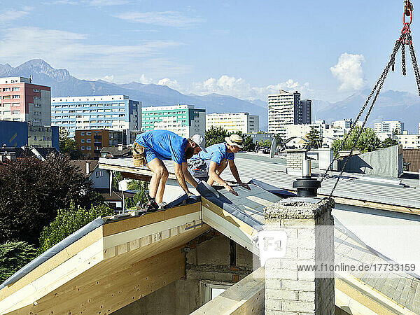 Workers installing wooden plank on rooftop of house