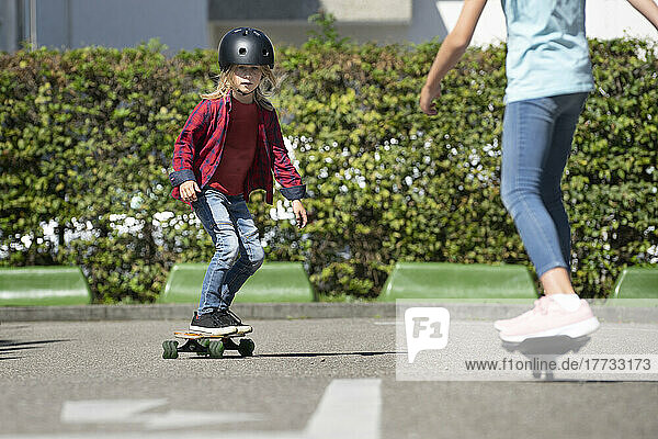 Junge trägt Helm und fährt mit Freund auf der Verkehrsstrecke Skateboard