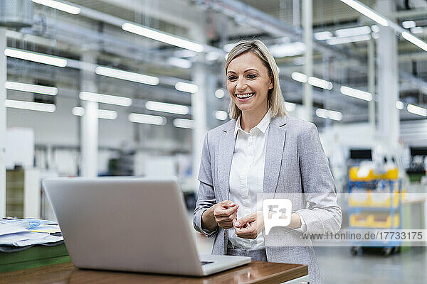 Happy businesswoman looking at laptop in factory