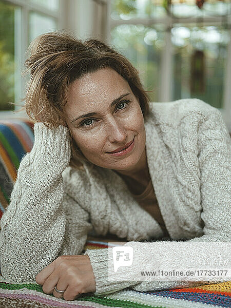 Smiling mature woman wearing sweater lying at home