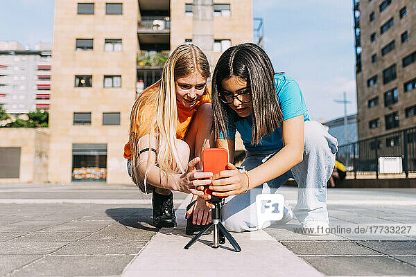 Smiling girls adjusting smart phone on tripod