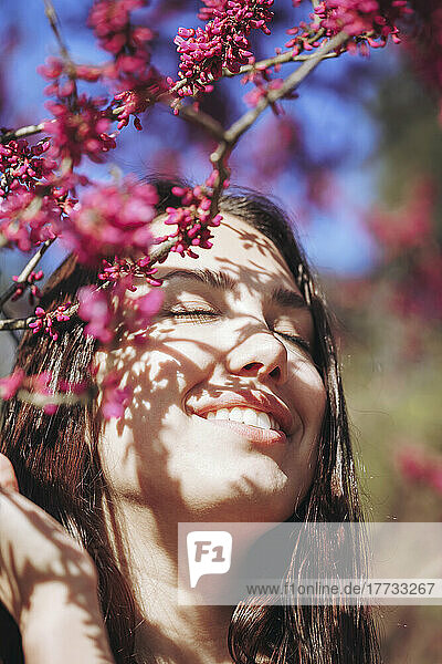 Glückliche junge Frau mit geschlossenen Augen durch rosa Blumen