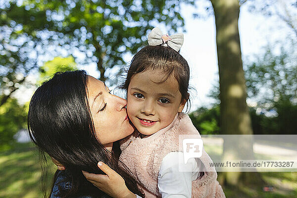 Mother kissing daughter in park on sunny day