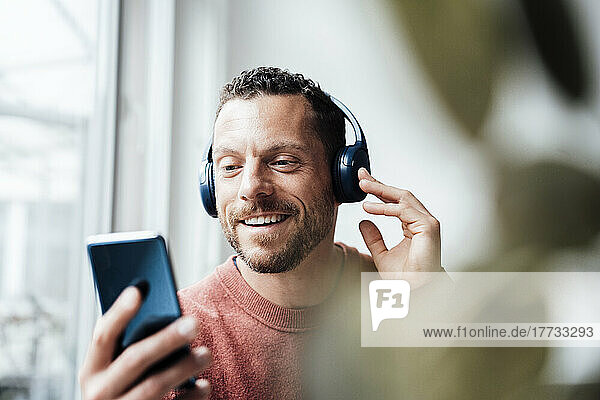 Smiling man with headphones using smart phone at home