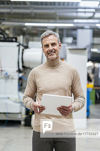 Lächelnder Geschäftsmann hält digitales Tablet in der Fabrik