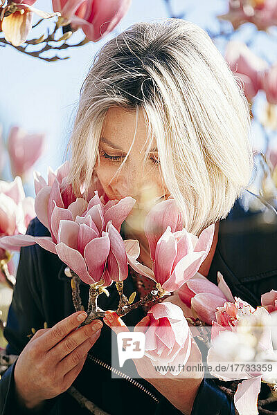 Smiling woman smelling pink flowers on sunny day