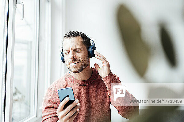Man holding smart phone enjoying music on headphones at home