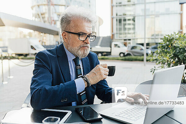Businessman with laptop drinking coffee sitting at sidewalk cafe