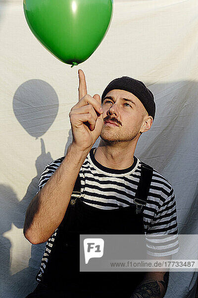 Man playing with green balloon in front of white backdrop