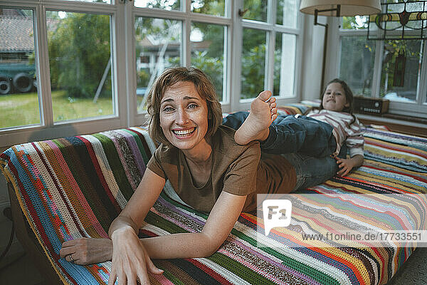 Smiling mature woman with playful daughter lying on sofa at home