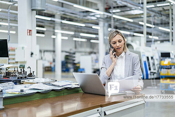 Businesswoman with laptop on the phone in factory