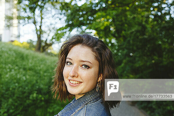 Smiling teenage girl wearing denim jacket in park