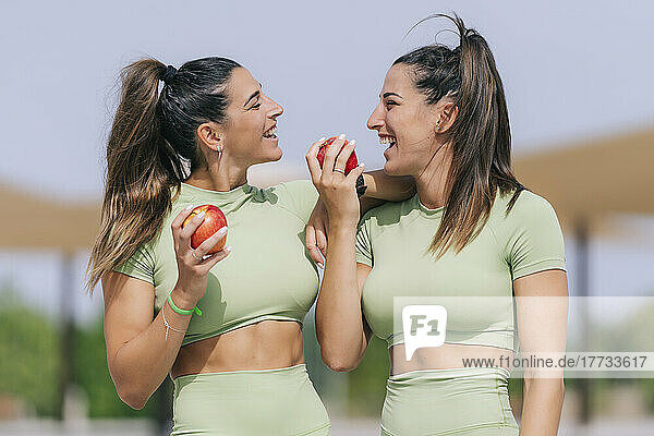 Happy young woman with twin sister holding apple on sunny day