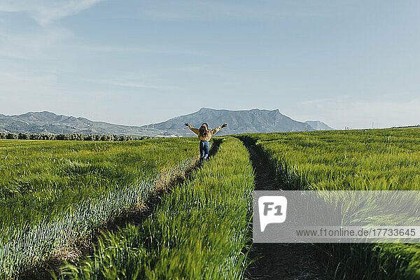 Frau mit ausgestreckten Armen läuft an einem sonnigen Tag inmitten von Gras auf einer Wiese