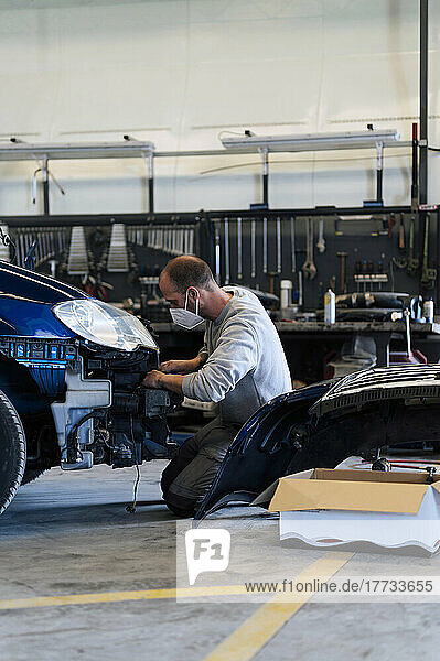 Auto mechanic kneeling and repairing car in garage