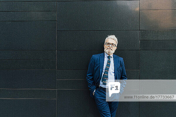 Smiling senior businessman standing in front of wall