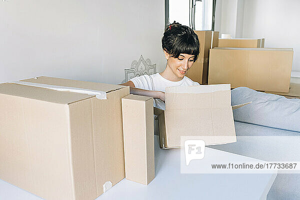 Woman looking in cardboard box sitting at table in living room