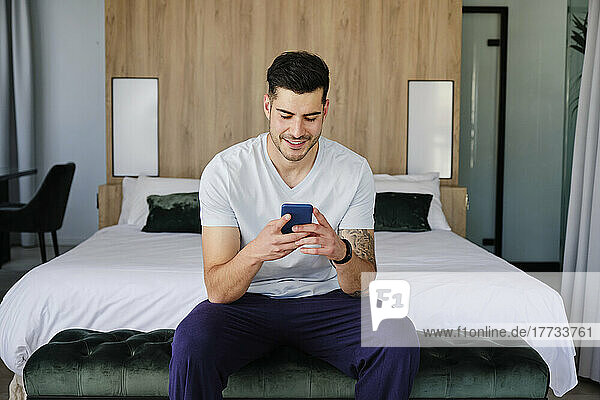 Young man using smart phone in bedroom at home