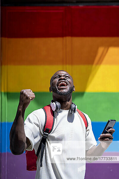 Happy young man screaming in front of rainbow wall