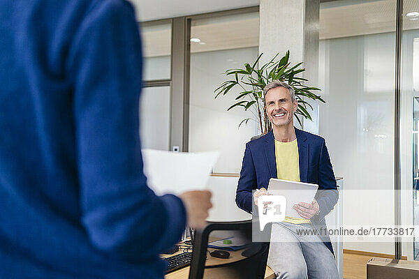 Smiling businessman with digital tablet looking at businesswoman in office