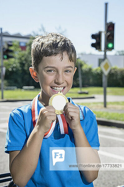 Smiling boy showing golden medal on sunny day