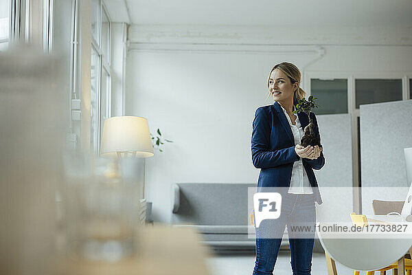 Smiling businesswoman holding plant in office