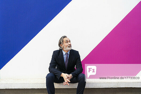 Businessman with hands clasped sitting in front of multi colored wall