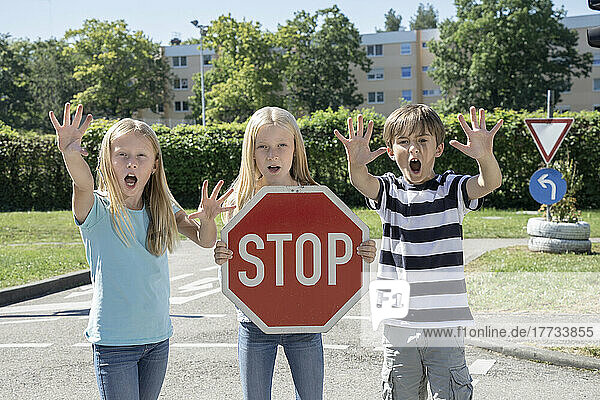 Girl holding stop sign board standing by friends on sunny day