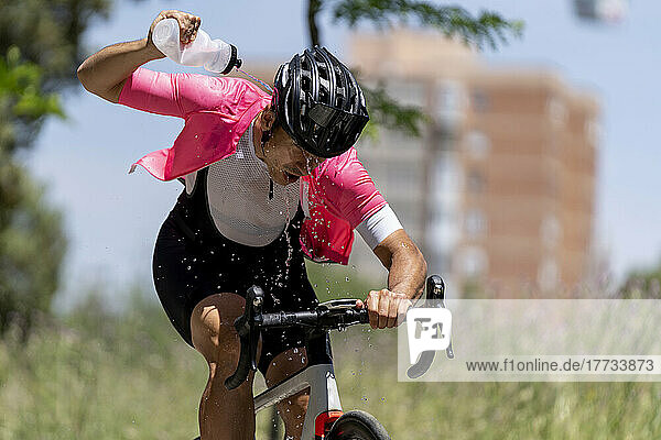 Radfahrer fährt Fahrrad und gießt an einem sonnigen Tag Wasser aus der Flasche