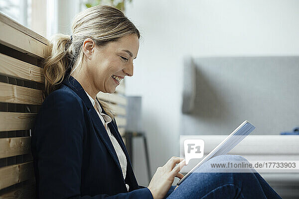 Happy businesswoman using tablet PC leaning on radiator in office