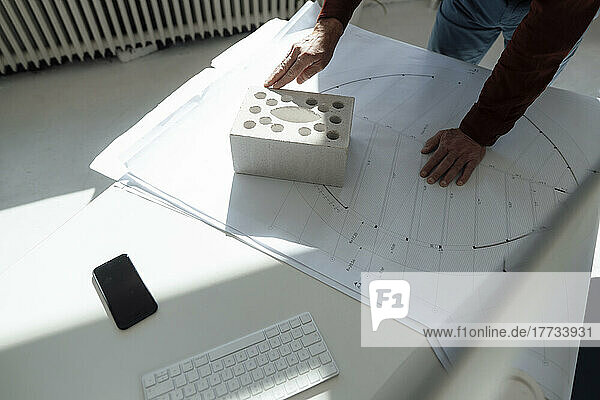 Hände des Architekten auf Betonstein und Bauplan am Schreibtisch