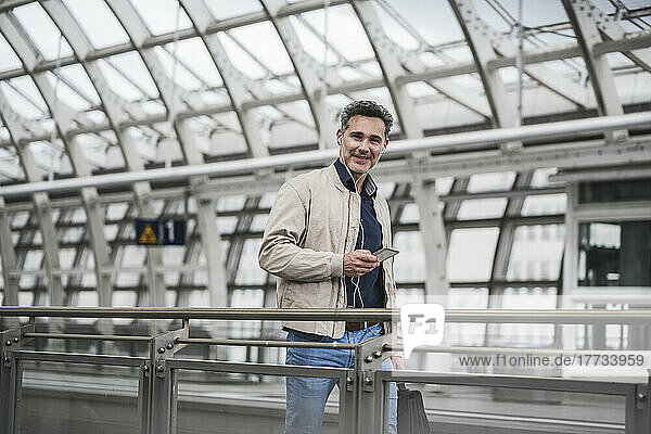 Smiling businessman with smart phone and bag walking at railroad station
