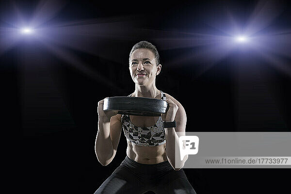 Smiling young woman lifting weight plate in fitness room