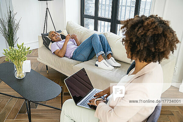 Happy patient lying on sofa discussing with psychologist in office