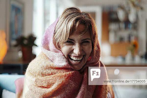 Cheerful woman wrapped in blanket sitting at home